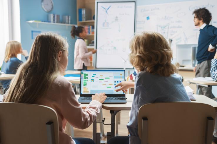 Two students in a classroom looking at learning materials on a laptop. 