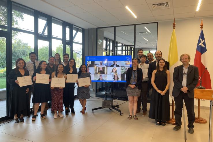 A group of people stand together, holding diplomas.