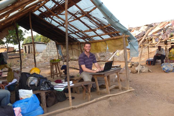 A man works at a laptop under a tin roof