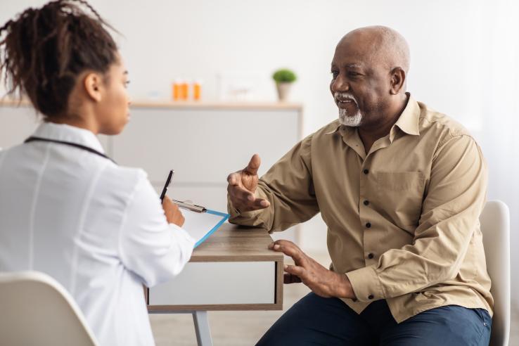 A Black Principal Investigator sitting at a table speaking with a Black older man