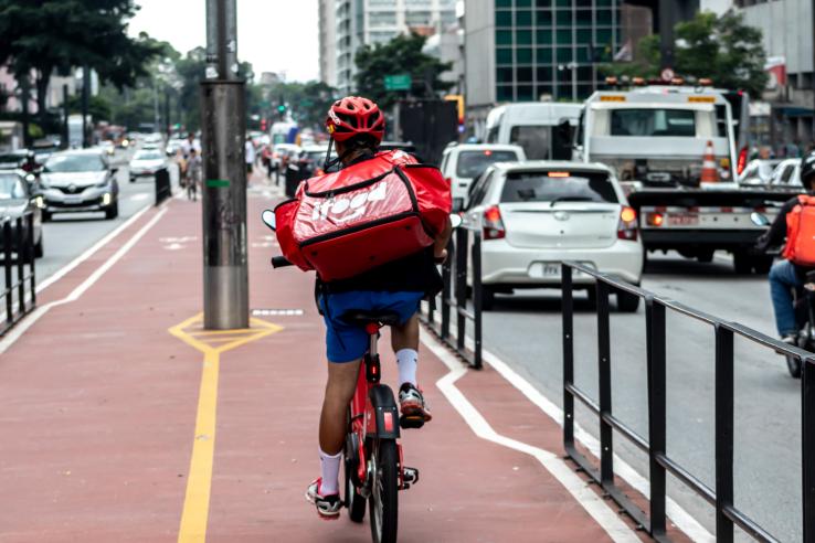 A man rides a bicycle with a red food delivery backpack.