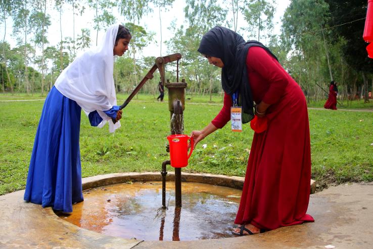 Two female students collect clean water from a tube well in a jug in Bangladesh.