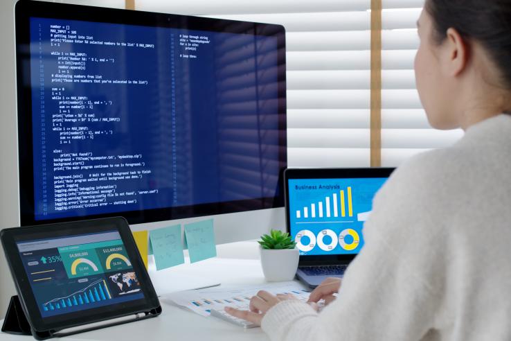 Person seated at a desk working in front of multiple monitors.