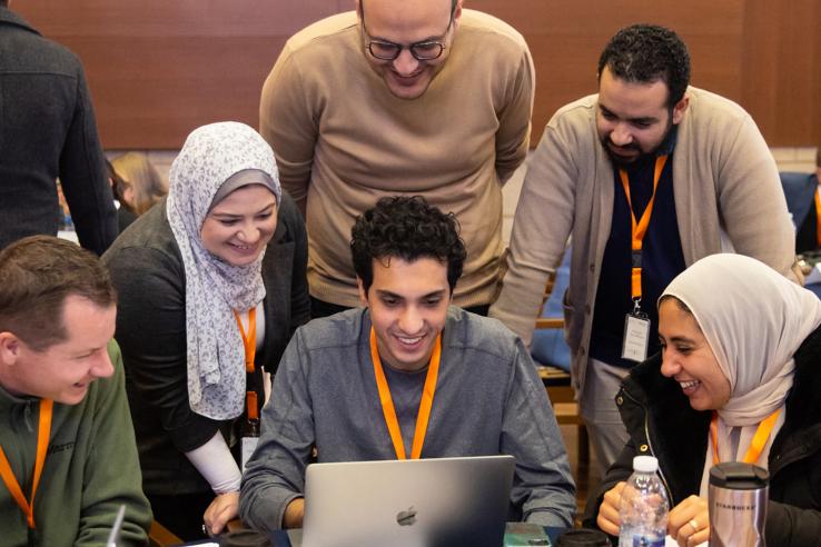 Students smiling while gathered around a laptop during a training