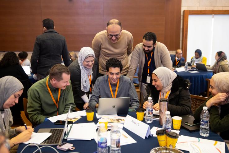 Students smiling while gathered around a laptop during a training