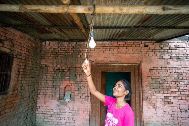 A smiling woman pulls a cord, turning on a lightbulb. 