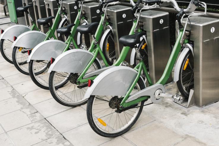 A row of green and grey e-bikes charge at an outdoor station