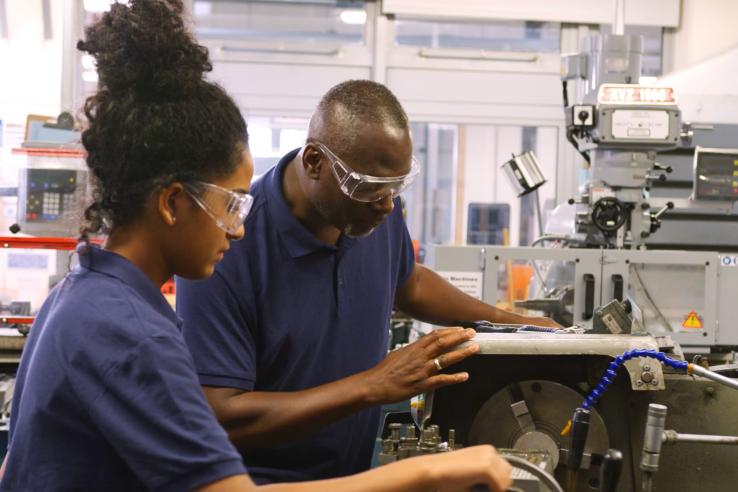 Student working on machinery in a shop with an instructor