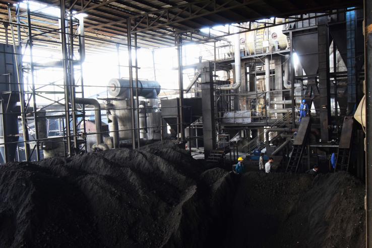 workers stand behind large piles of coal at an industrial plant