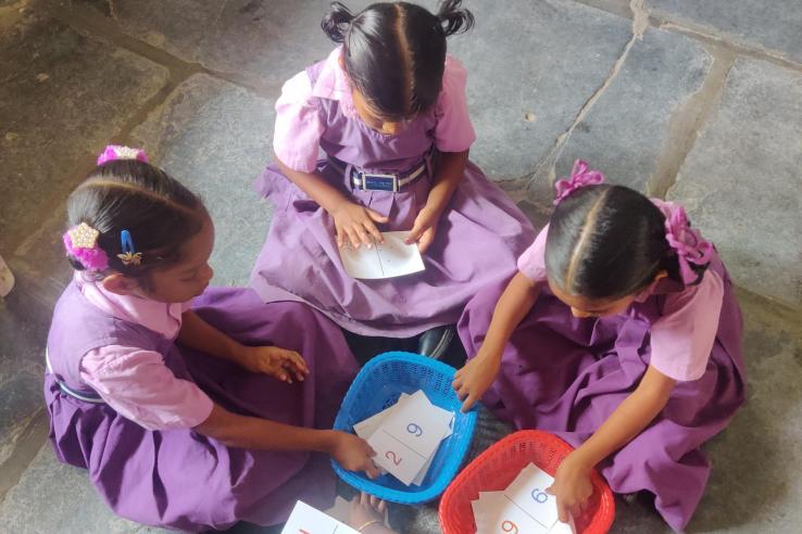Three young children sitting on ground reaching for math cards