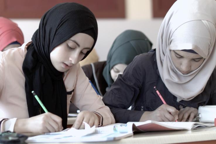 Two young Syrian girls writing in notebooks while at school