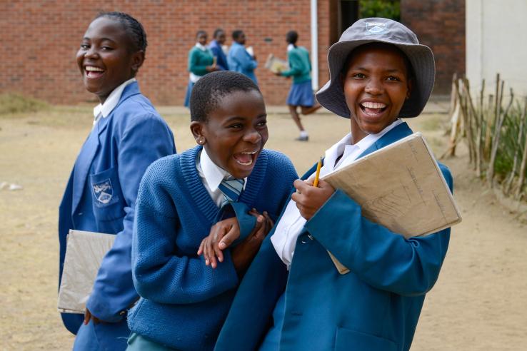 Three students laugh while standing in front of a school