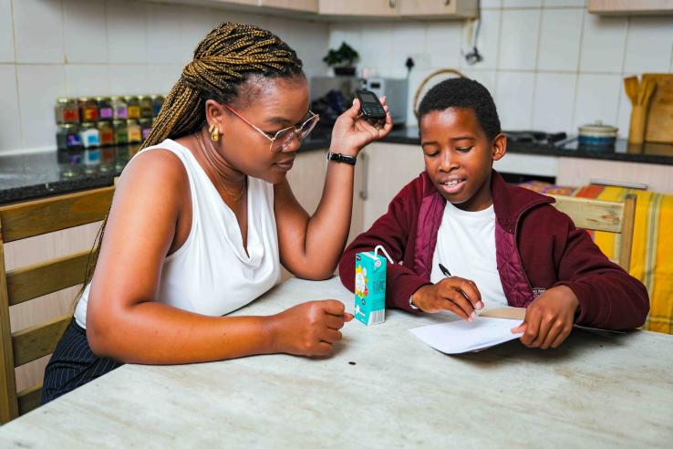 A woman sits at a table with a boy looking at a sheet of paper.