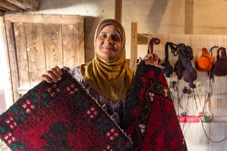 Woman wearing a headscarf holding up a rug