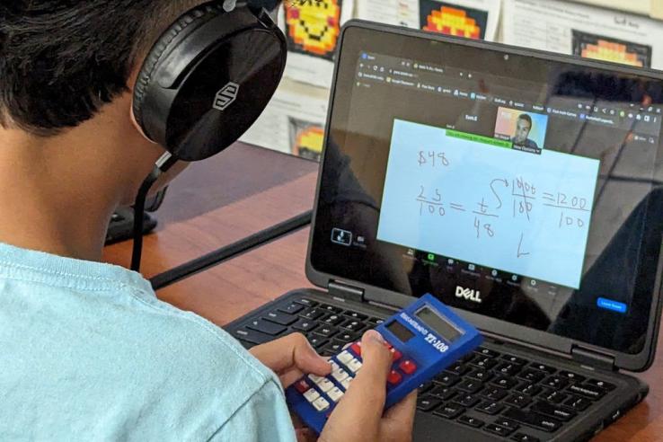 Student with headphones looks at computer screen with mathematical equation while typing on keybord 