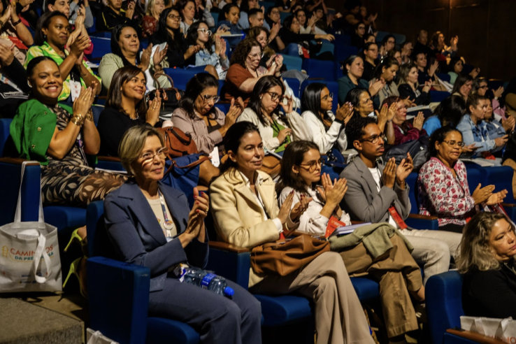Women sit dressed in business casual clothing and applauding in an auditorium