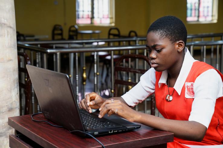 A student in a red and white school uniform types on a computer
