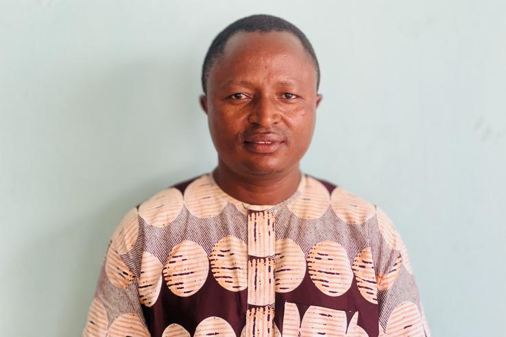 A man stands in a sweater in front of a light blue wall.