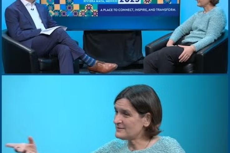 Esther Duflo sits in a blue shirt with a man in a blue suit, facing each other