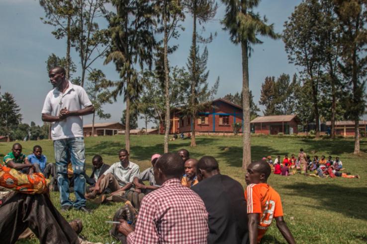 A man presents to a group of young men with palm trees in the background.
