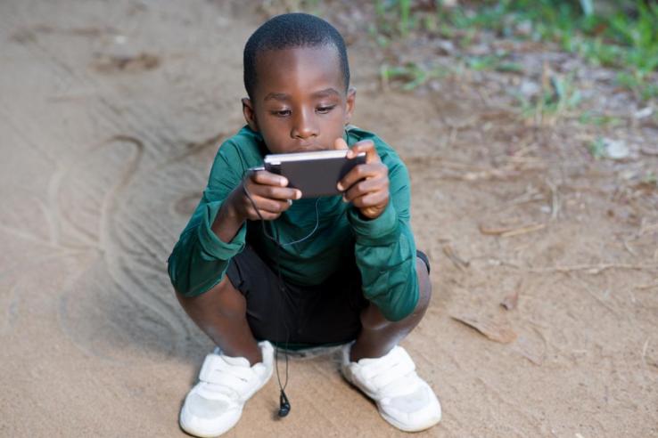 A young boy squats in road engaging with a mobile phone