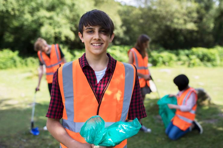 Teens in orange vests collect litter in the countryside.