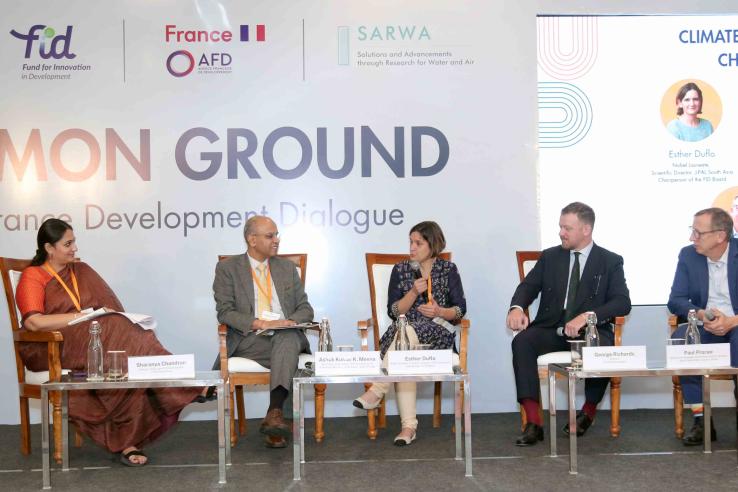 Five panelists seated on stage during the “Common Ground: India–France Development Dialogue” session on climate and resilience, with Esther Duflo speaking into a microphone while the others listen.