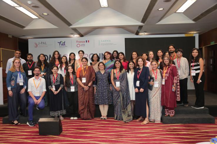 Group photo of about 30 members of the J-PAL South Asia, AFD and FID teams posing together on a stage with Esther Duflo, who stands near the centre in a navy printed kurta. Most wear event lanyards, and some in the back row stand on a raised step. Behind them is the “Common Ground” backdrop with the J-PAL South Asia, FID, AFD and SARWA logos.