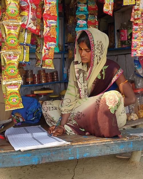 A woman sits in her shop and writes in a notebook.