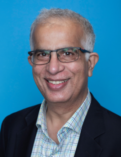 Adnan Khan smiles in front of a blue wall