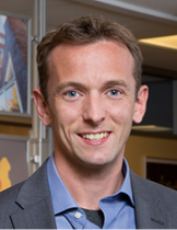 Headshot of Martin Abel wearing a blue shirt and grey blazer