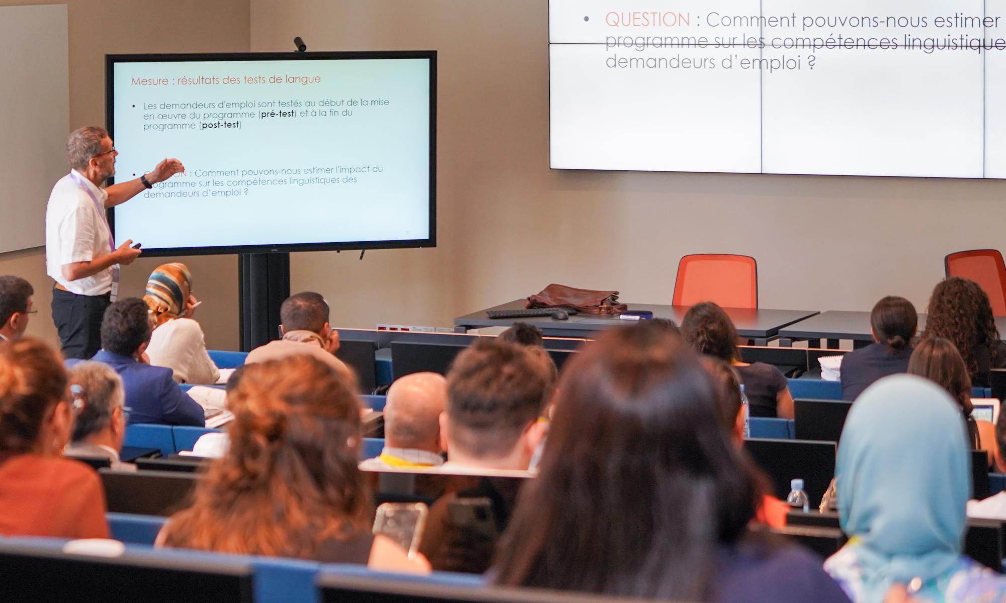 Speaker pointing to slide in front of large classroom