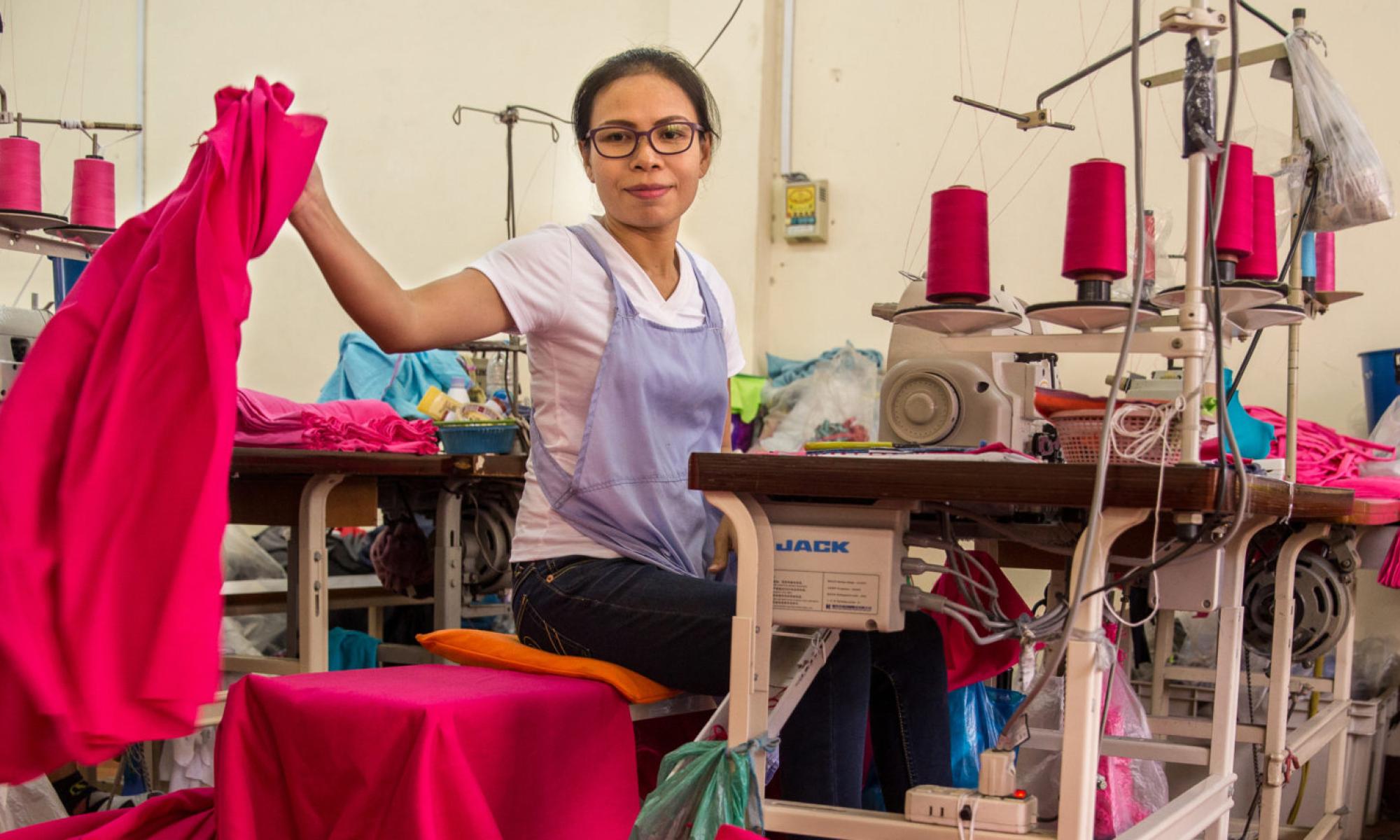 Woman placing a sewn skirt on the ground while sitting at her sewing machine