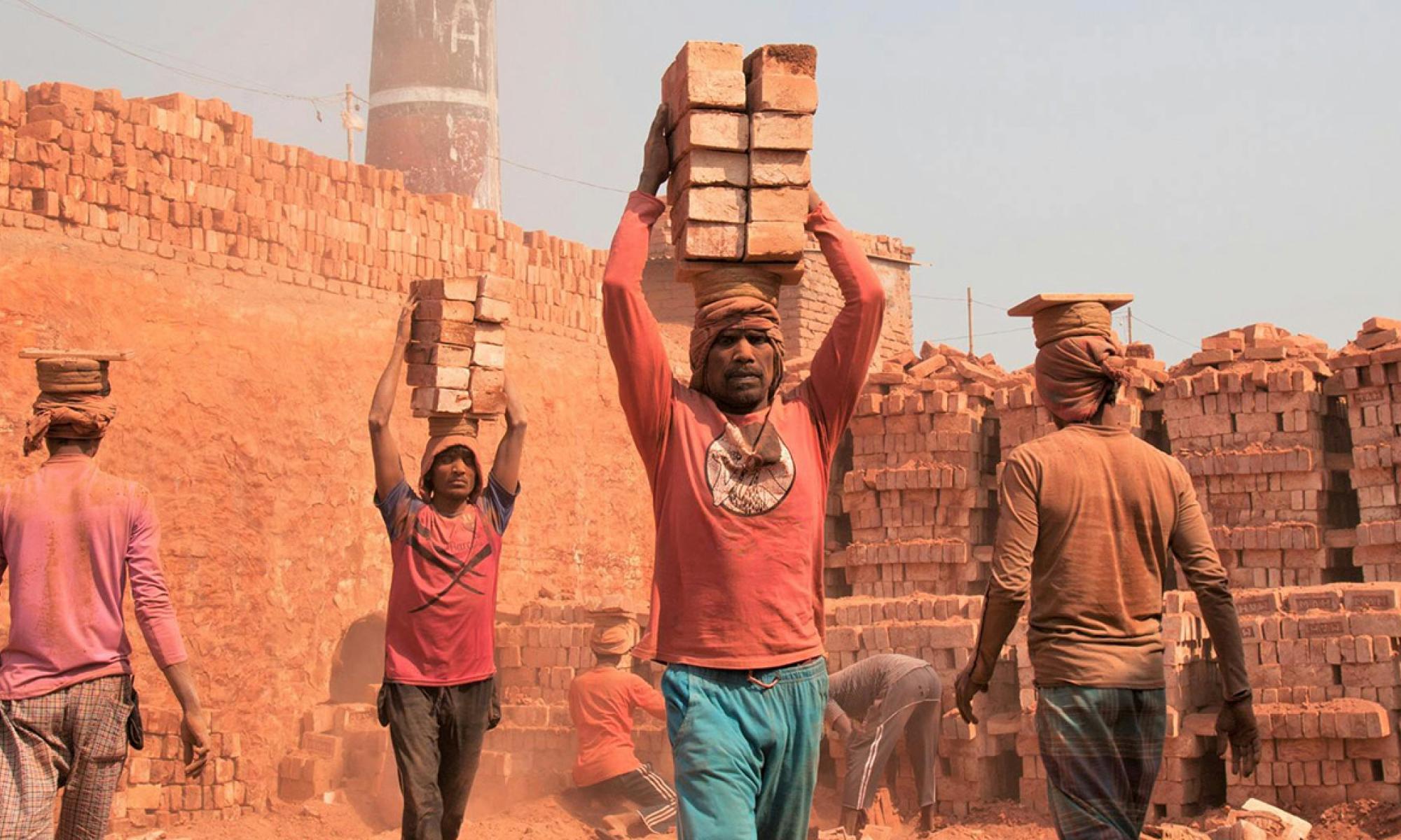Four men walking with bricks on their heads in a brick manufacturing plant