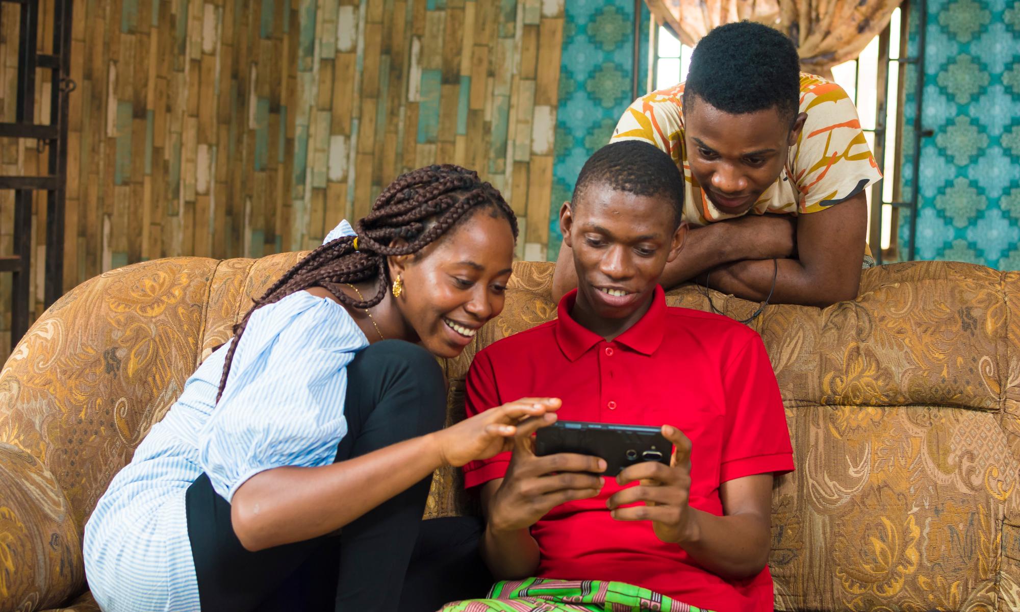 A young woman and two men smile while watching a show on a phone. 