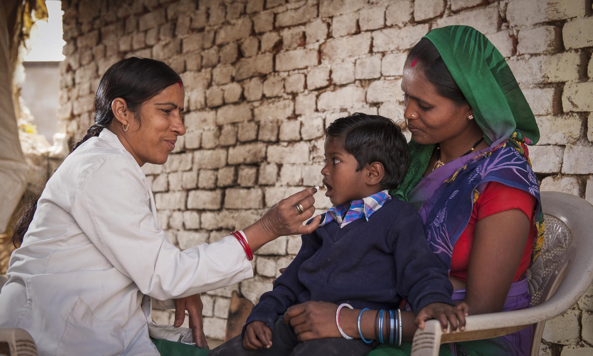 Health provider handing a deworming pill to a child sitting on mother's lap