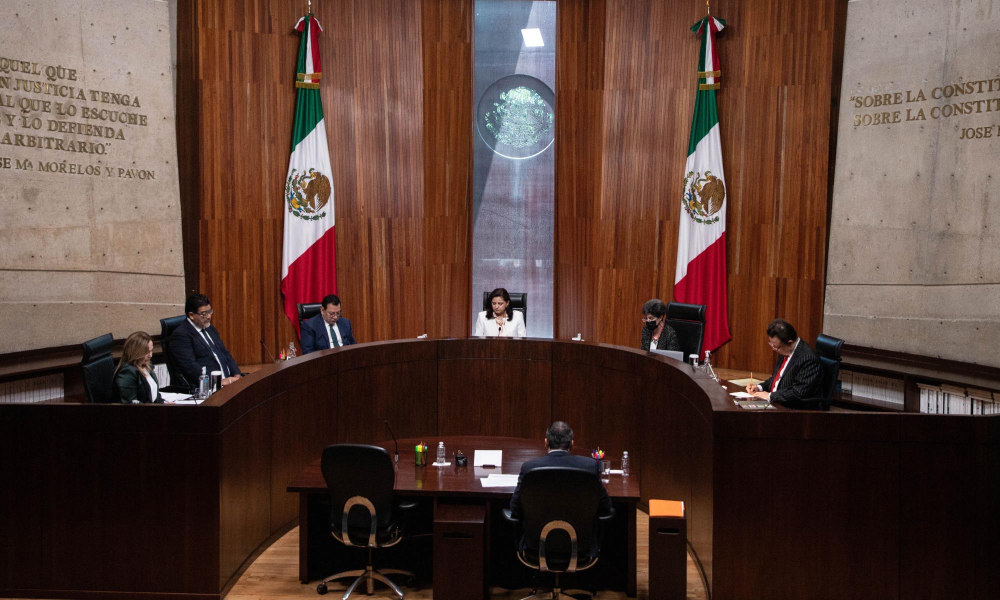 Five people sit around an oval bench in front of another individual in a courtroom in Mexico City