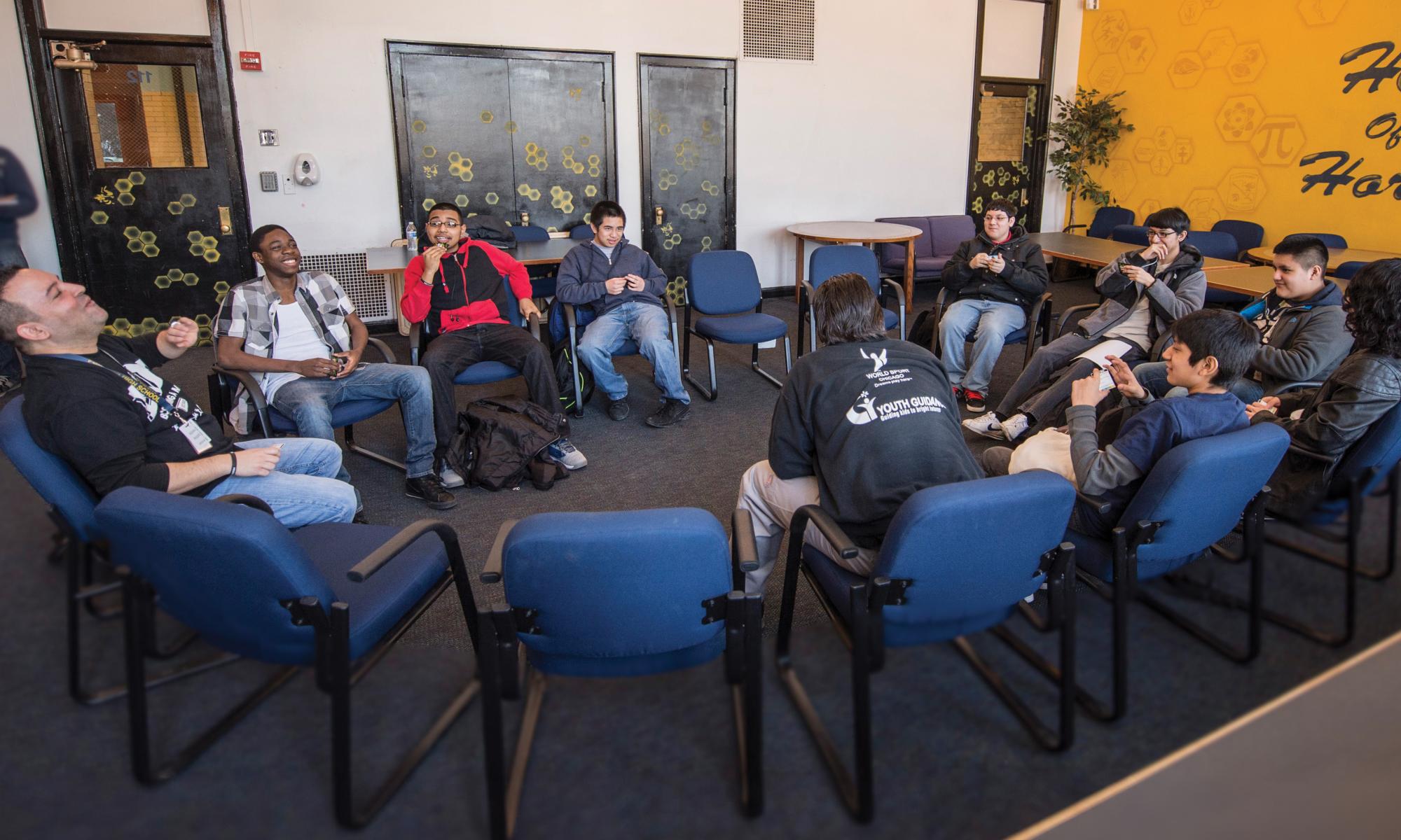 Group of students sit in a circle laughing with two adult group leaders