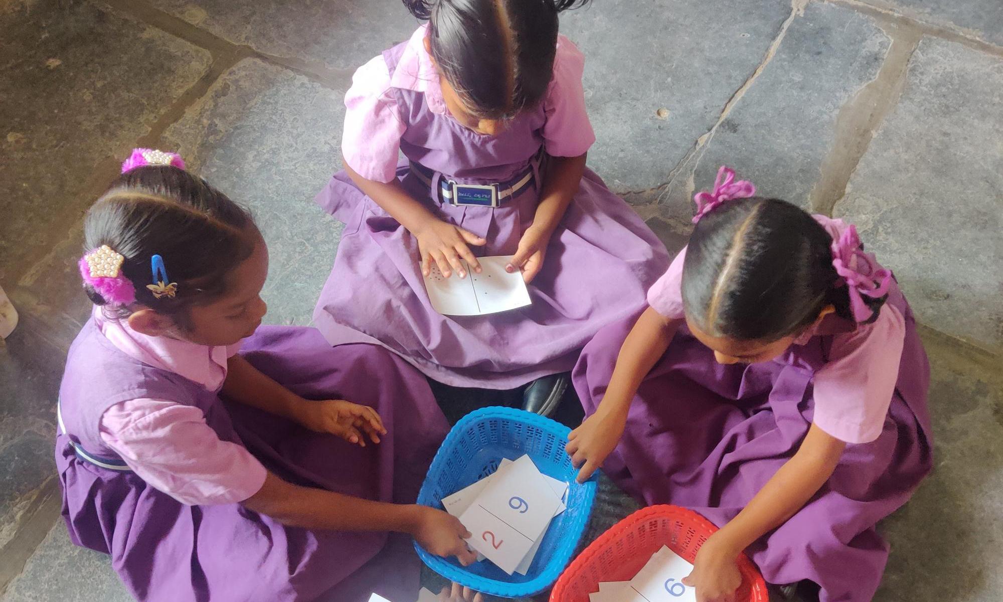 Three young children sitting on ground reaching for math cards