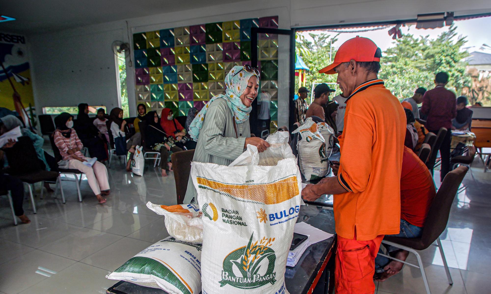 Woman smiles as we collects rice from a busy community hall