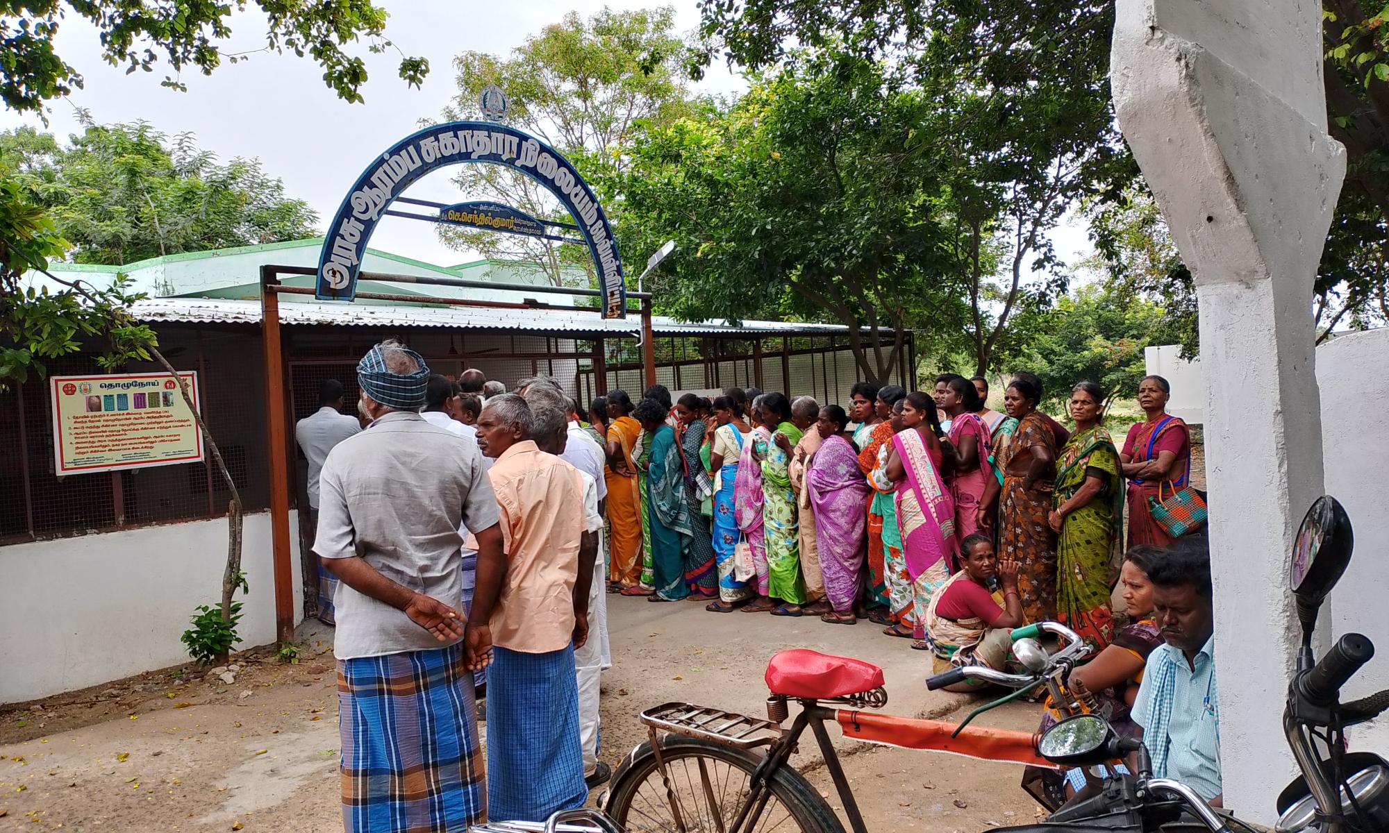 Men and women stand in line outside of a government health facility
