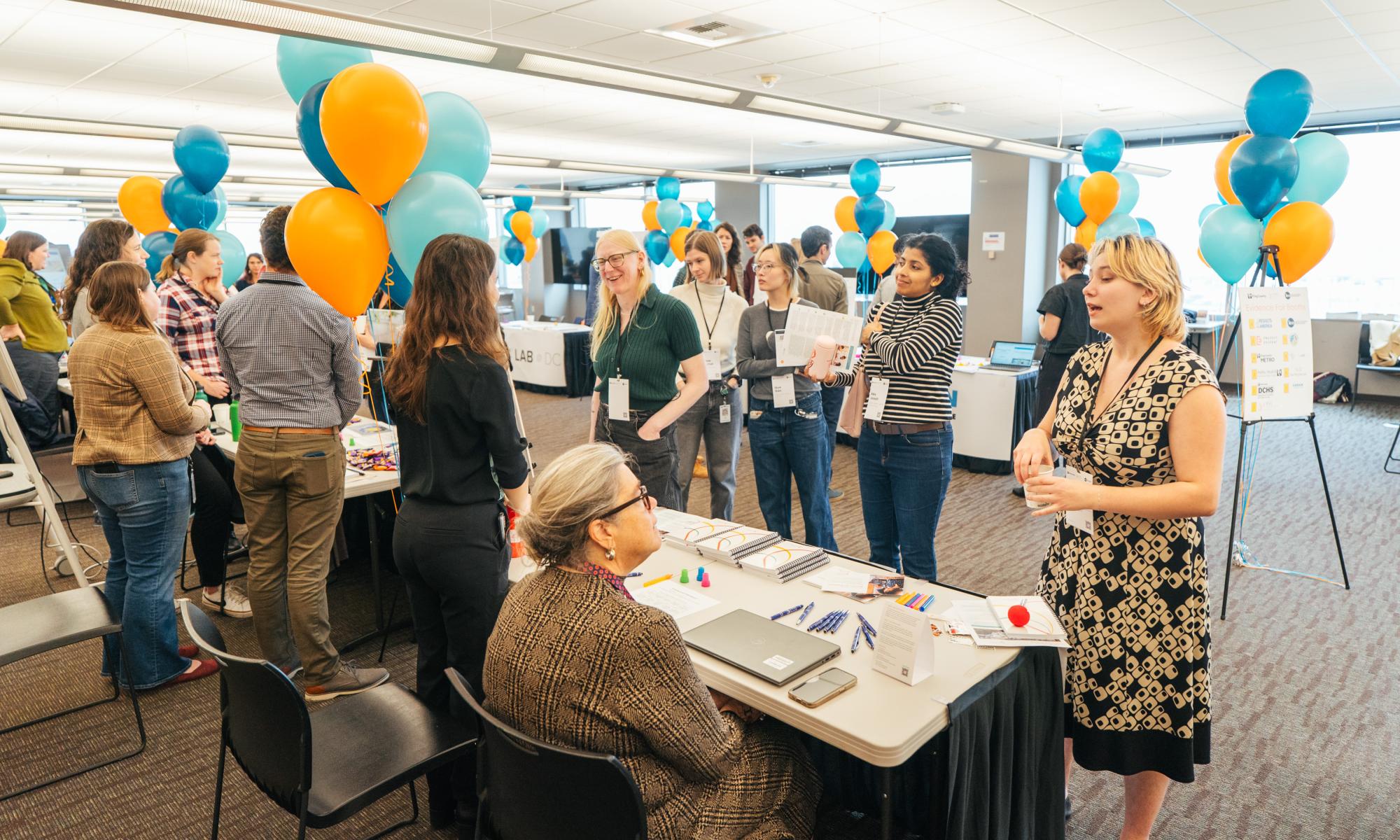 several people stand around J-PAL North America table at a convening