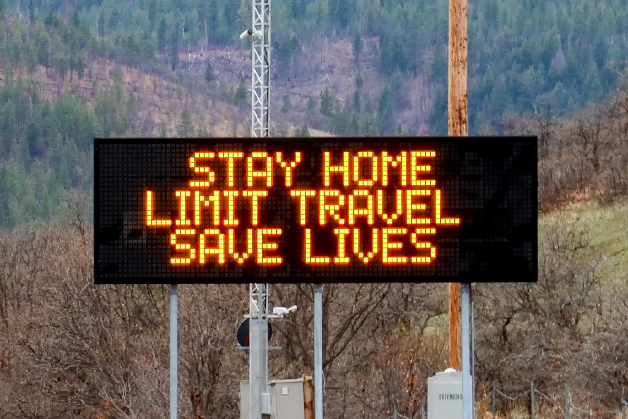 A roadside billboard that reads "stay home, limit travel, save lives"