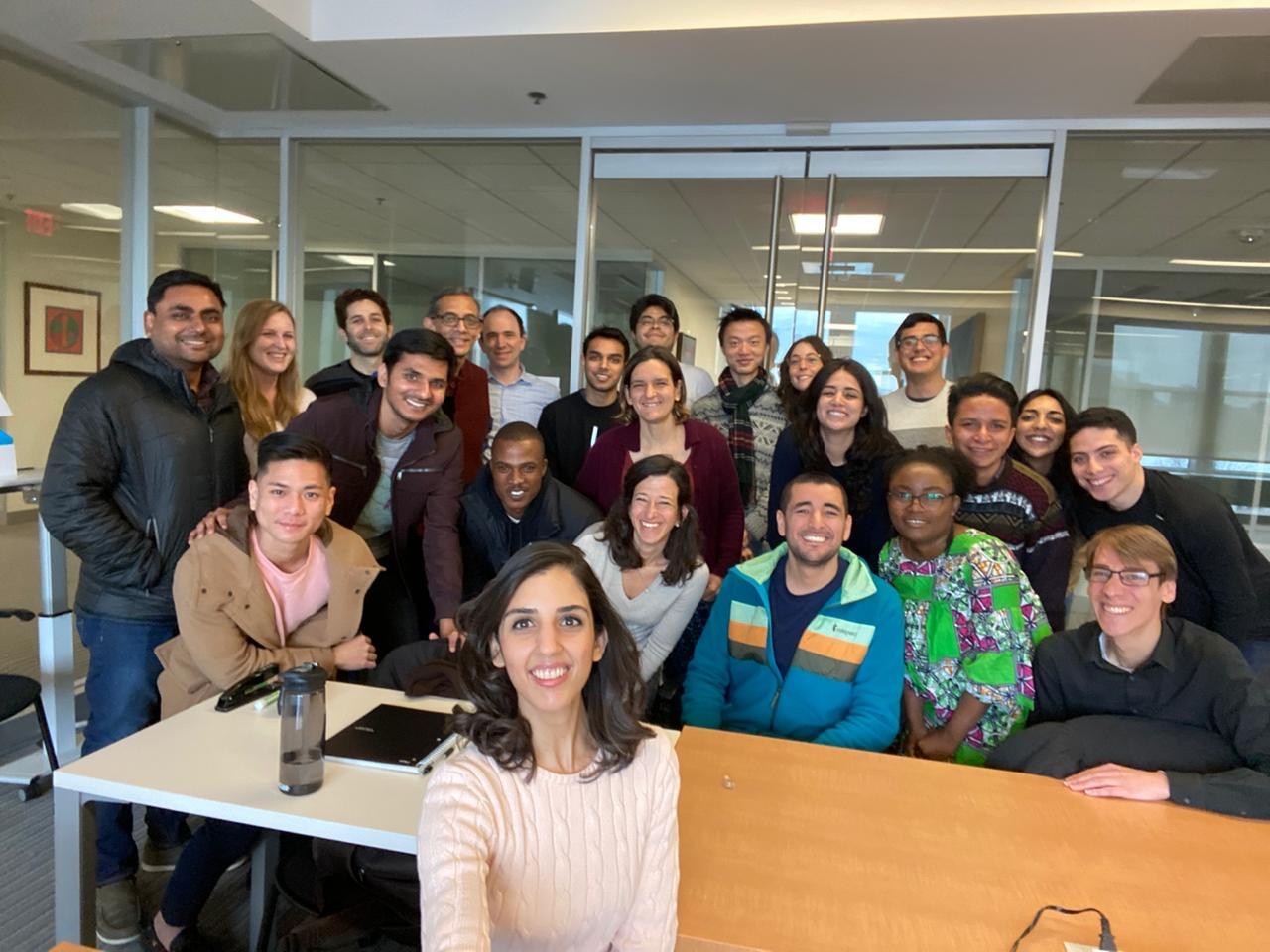 A group of DEDP master's students stand behind a table in an MIT classroom.