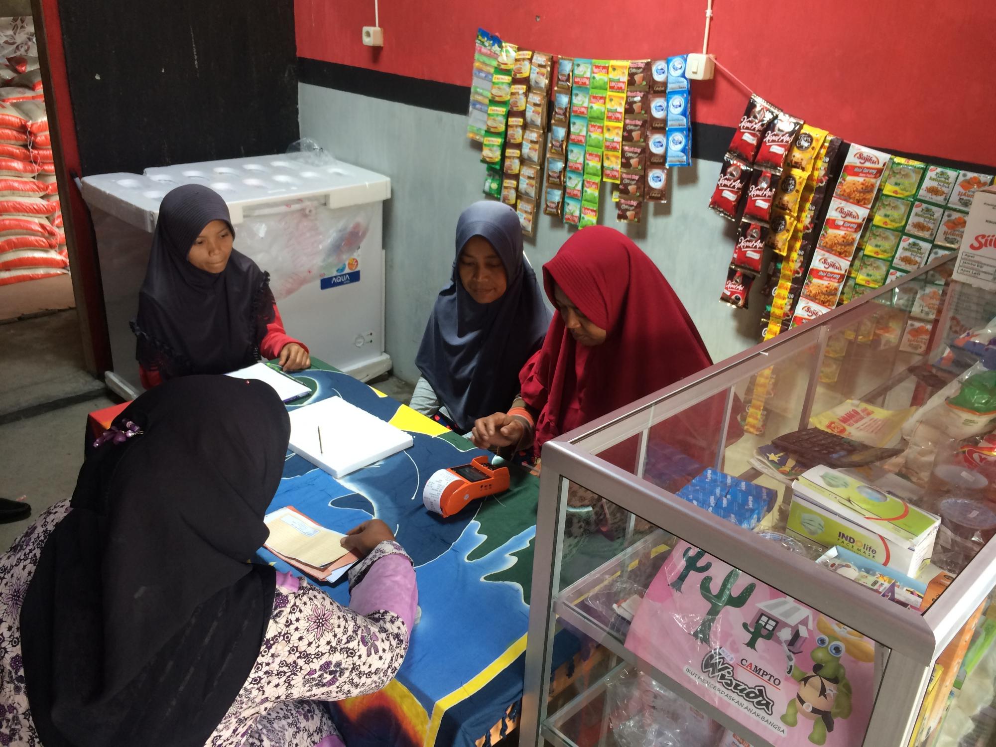 Four women group around a counter at a small shop. One woman is performing a transaction on a digital card reader.