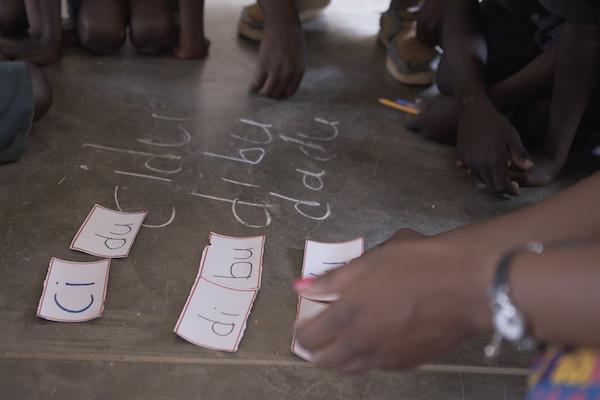 A teacher places phonetics cards on the floor.