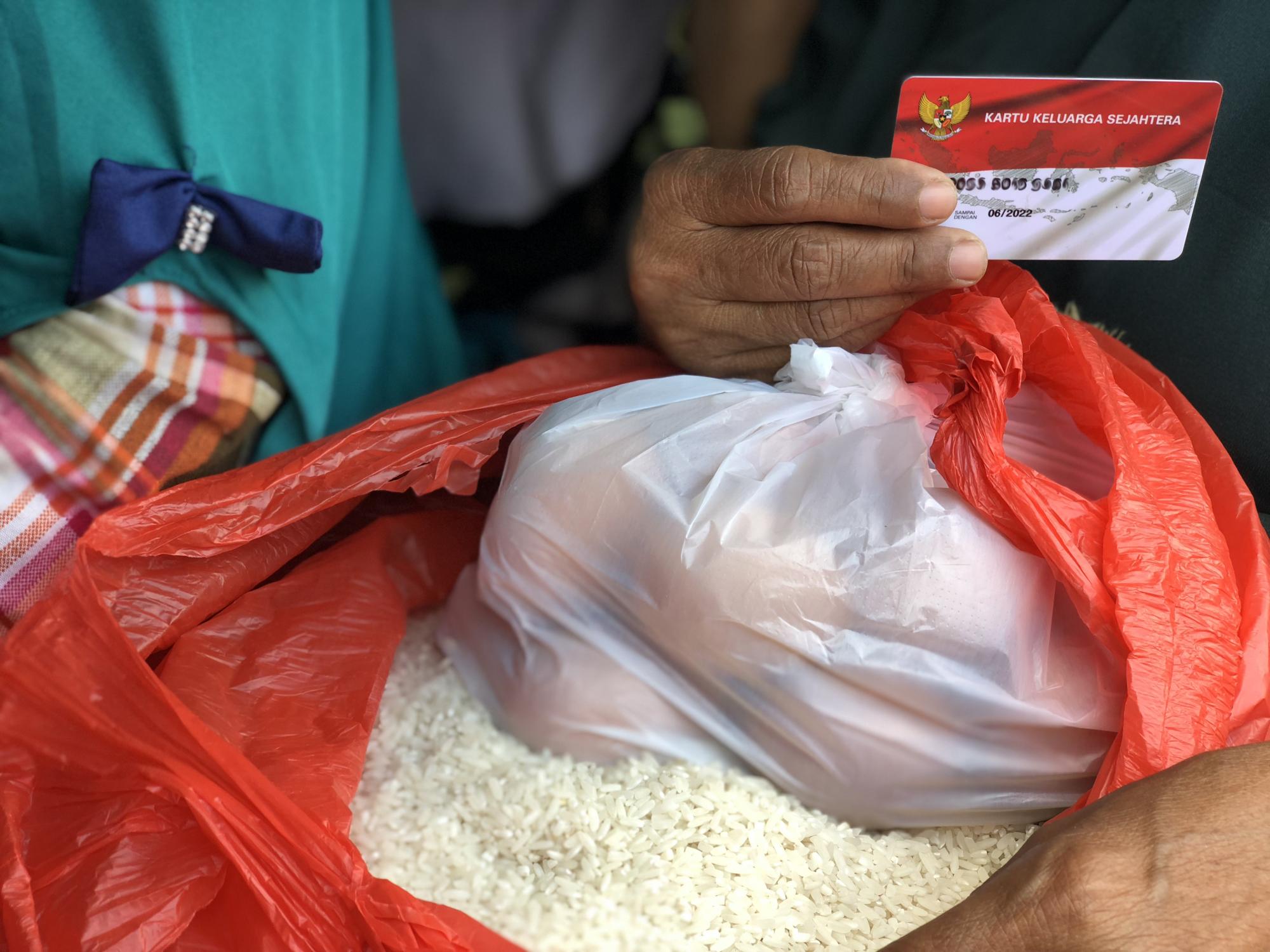 A hand holding a small card resting on top of a bag of rice and a bag of fruit.