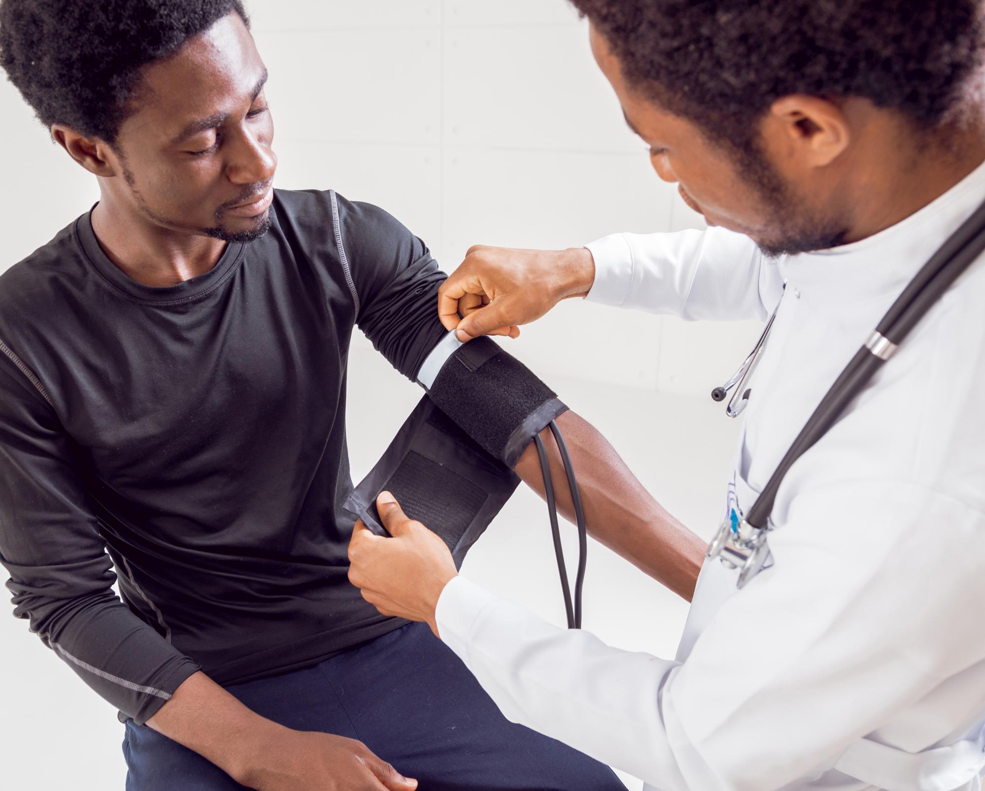 A Black doctor takes the blood pressure of a seated Black man