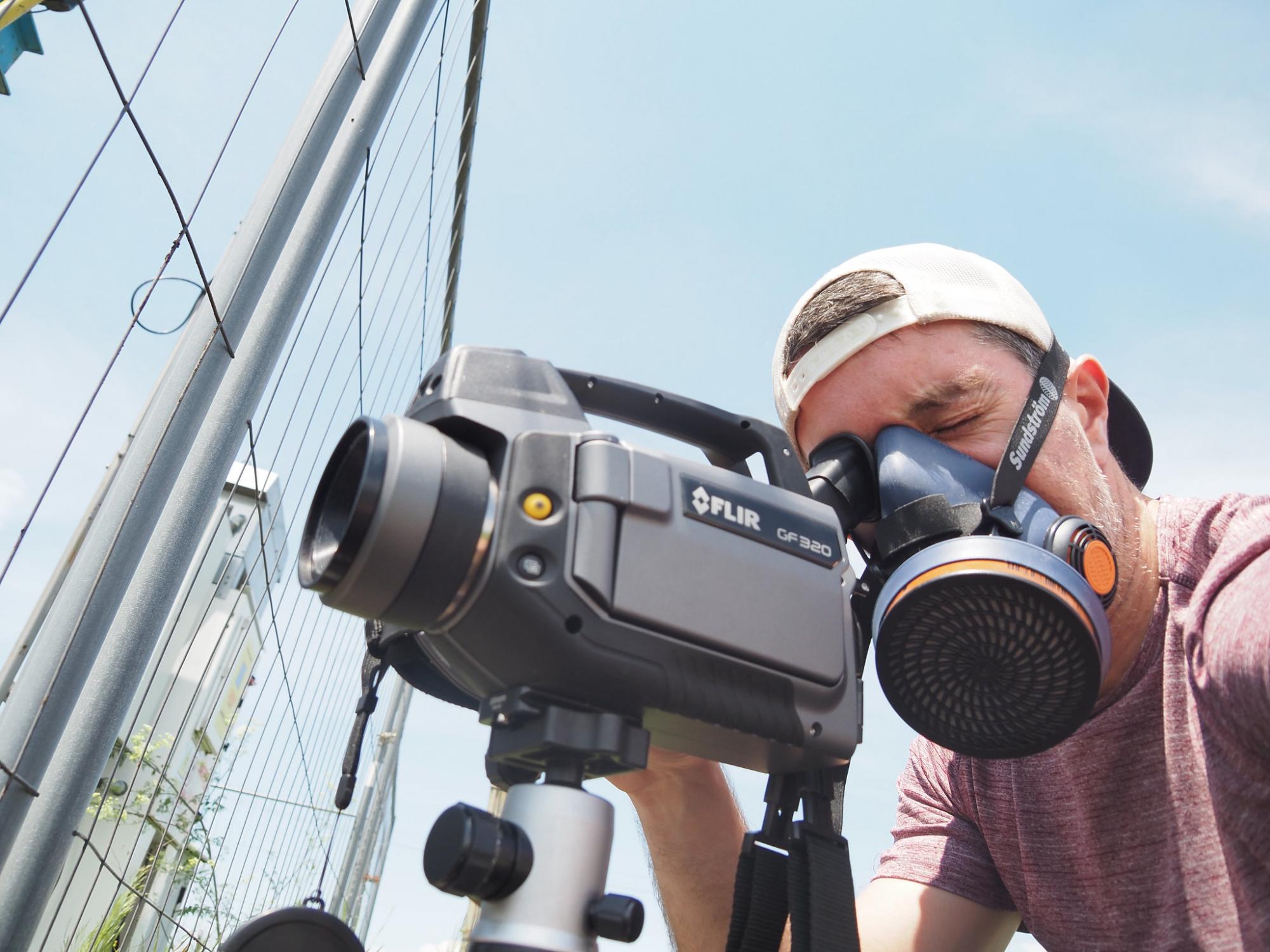 James, wearing a gas mask, looks at an oil well through a camera 