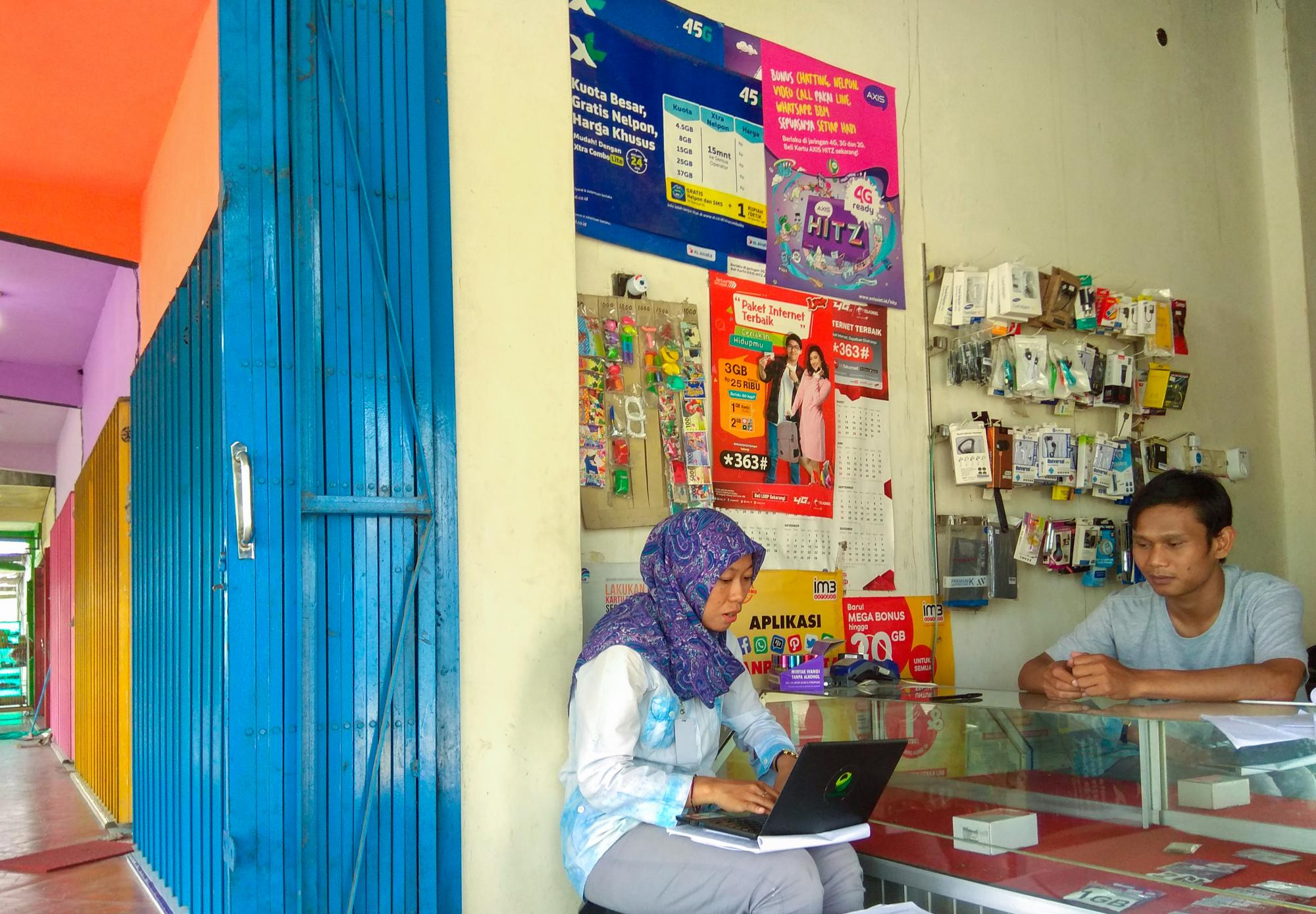 Researcher conducts a branchless banking evaluation spot check with an Indonesian shop owner.
